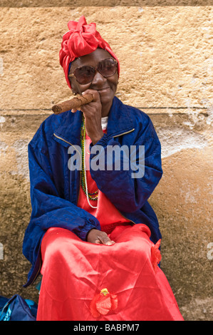 Femme âgée dans une coiffe rouge fume un gros cigare dans la Habana Vieja. Banque D'Images