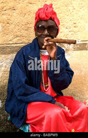 Femme âgée dans une coiffe rouge fume un gros cigare dans la Habana Vieja. Banque D'Images