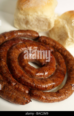 Une assiette de grillades de saucisses boerewors agriculteurs sud-africain dans sa spirale traditionnel avec des petits pains à l'arrière-plan Banque D'Images