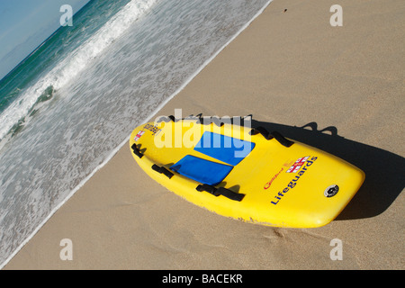 Jaune de la RNLI Sauveteur sauvetage planche de surf sur la plage de sable de Sennen Cornwall avec l'océan Atlantique mer Banque D'Images