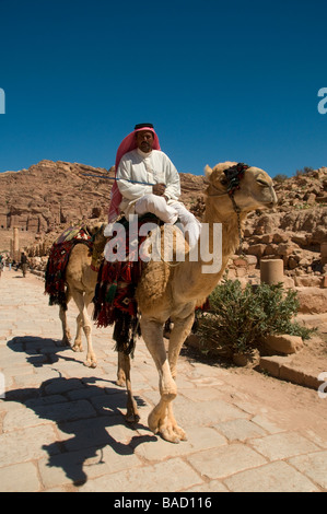 Un homme portant un keffieh à carreaux blancs et rouge monté sur un chameau dans l'ancienne ville nabatéenne de Pétra en Jordanie Banque D'Images