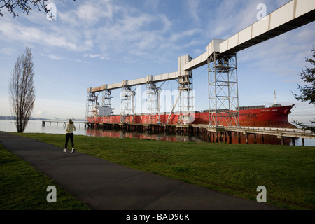 Woman Running à Myrtle Edwards Park Cargo Navios espère amarré au port de Seattle de grain dans l'arrière-plan Banque D'Images