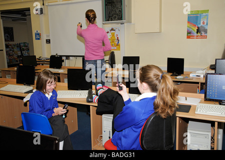 Ecolières en utilisant un téléphone portable dans une salle de classe pendant que l'enseignant n'est pas à la Banque D'Images