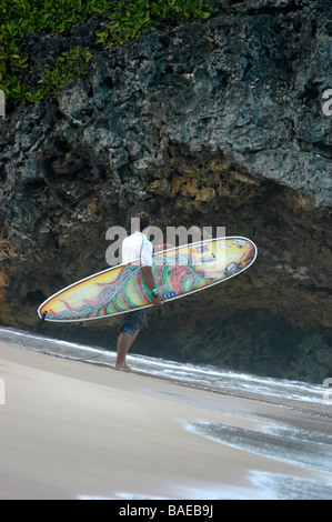 Un surfeur debout sur la plage en tenant son administration à de hautes roches avant d'entrer dans la mer Banque D'Images