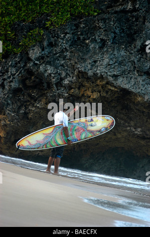 Un surfeur debout sur la plage en tenant son administration à de hautes roches avant d'entrer dans la mer Banque D'Images