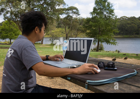 Jeune homme travaillant avec un ordinateur portable sur la table à l'extérieur du parc Banque D'Images