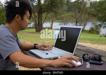 Jeune homme travaillant avec un ordinateur portable sur la table à l'extérieur du parc Banque D'Images