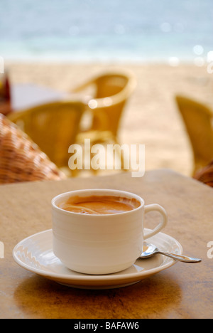 White tasse de café et soucoupe sur la table en bois avec chaises en osier, plage, et la mer en arrière-plan flou Banque D'Images