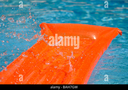 Éclaboussé de l'eau sur un lit d'air orange flottant dans une piscine. Banque D'Images