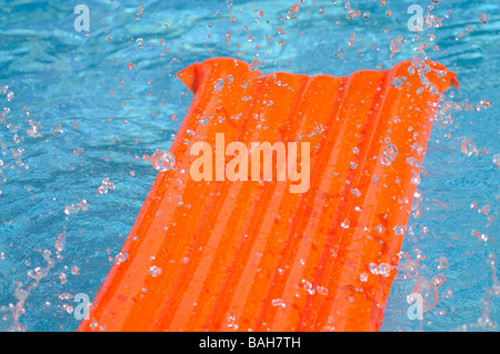 Éclaboussé de l'eau sur un lit d'air orange flottant dans une piscine. Banque D'Images