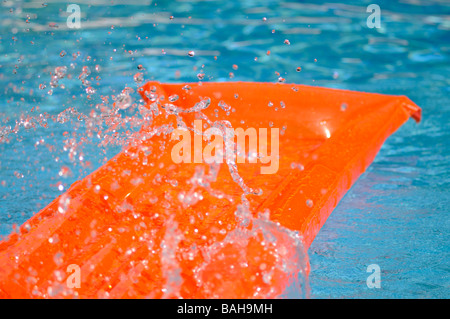 Éclaboussé de l'eau sur un lit d'air orange flottant dans une piscine. Banque D'Images