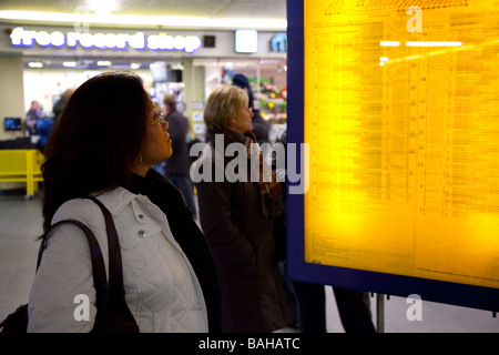 Femme debout devant la gare de circuit d'affichage à la recherche à des départs. Banque D'Images