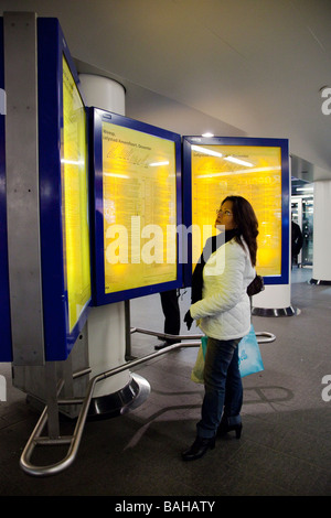 Femme debout devant la gare de trains en partance pour l'affichage de l'itinéraire, Amsterdam, Pays-Bas. Banque D'Images