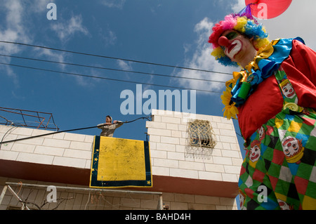 Une palestinienne regarde un colon juif en costume de clown pendant la fête juive de Purim dans la ville divisée de Cisjordanie d'Hébron Israël Banque D'Images