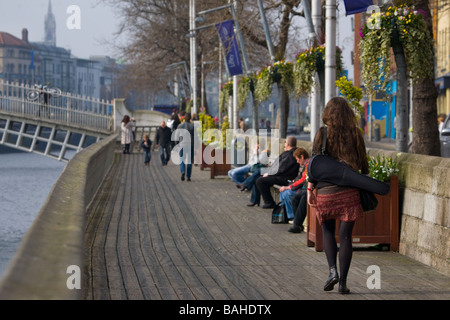 Fille aux cheveux rouges marchant sur la Liffey Boardwalk vers Ha penny Bridge Dublin exerçant son étui à violon Banque D'Images