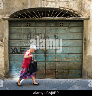 Une vieille dame aux cheveux blancs pour faire son shopping dans les rues de graffitied Lucca, Toscane, Italie Banque D'Images