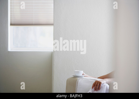 Femme assise dans un fauteuil avec une tasse et soucoupe, mid section Banque D'Images