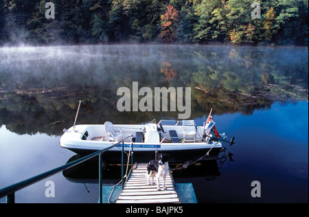 Réflexions brumeuses sur le Lot de la rivière et le stade d'atterrissage avec bateau amarré où le chien attend pour aller pêcher, Aveyron France Banque D'Images