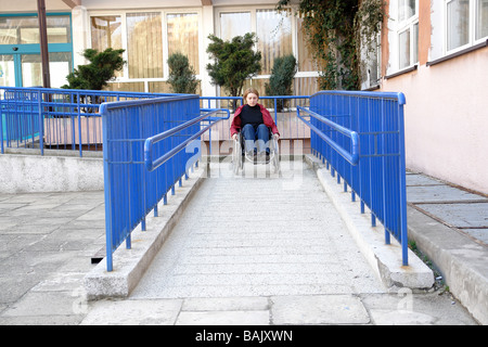 Femme handicapée sur fauteuil roulant quittent l'édifice à l'aide de rampe pour personnes à mobilité réduite Banque D'Images