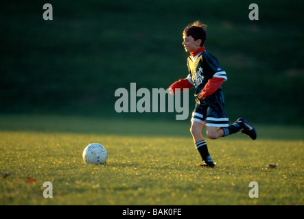 Jeune garçon dribble un ballon de soccer sur un terrain de jeu au coucher du soleil Banque D'Images