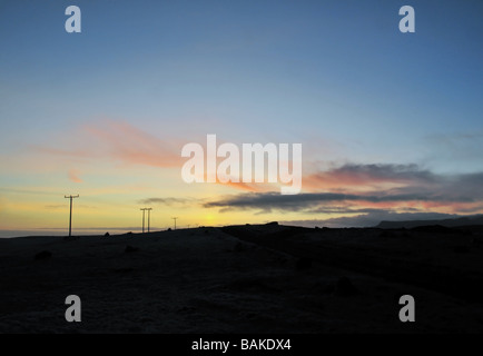 Une ligne d'alimentation en bois se dirigeant vers un coucher de soleil sur les collines à l'ouest de l'Islande du Sud, Brekkur Banque D'Images