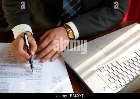 Homme assis à côté de l'écriture de l'ordinateur sur un document Banque D'Images