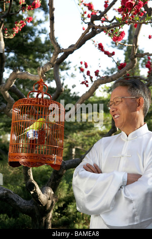 Chinese Man Looking At Bird In Cage Banque D'Images