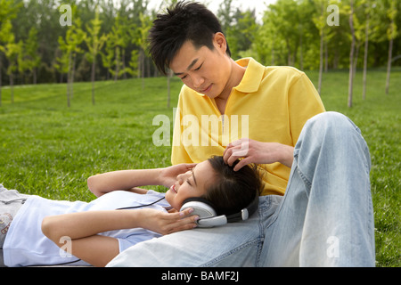 Jeune couple dans le parc portant sur le terrain avec des écouteurs Banque D'Images
