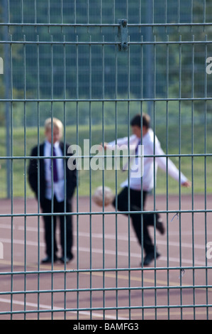 L'école de garçons jouant au football dans de jeu clôturé Banque D'Images