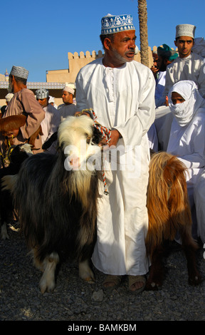 Les hommes habillés en costume traditionnel omanais le Dishdasha chèvre sur la place du marché, Nizwa, Sultanat d'Oman Banque D'Images