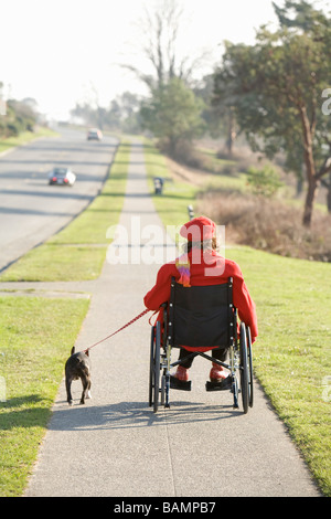 Femme en fauteuil roulant en tenant son chien pour une promenade Banque D'Images