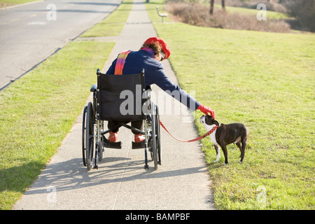 Femme en fauteuil roulant en tenant son chien pour une promenade Banque D'Images