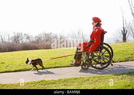 Femme en fauteuil roulant en tenant son chien pour une promenade Banque D'Images