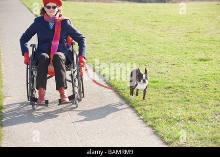 Femme en fauteuil roulant en tenant son chien pour une promenade Banque D'Images