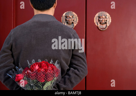Jeune homme en attente à l'avant porte avec un bouquet de roses derrière son dos Banque D'Images