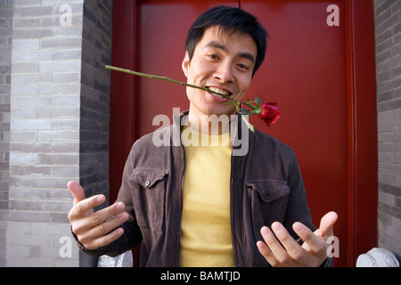 Jeune homme aux gestes à l'extérieur de porte tenant une rose dans sa bouche Banque D'Images