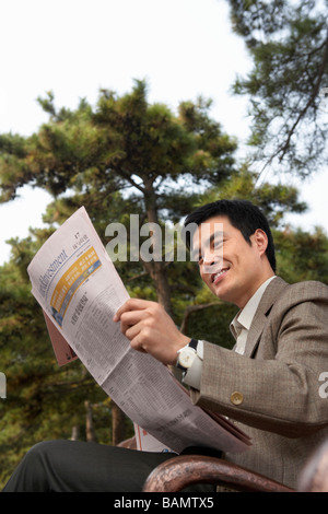 Businessman sitting on a park bench lire le journal Banque D'Images