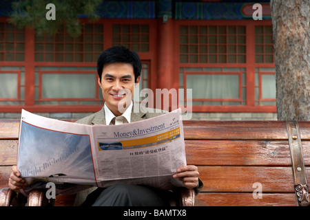 Businessman sitting on a park bench lire le journal Banque D'Images