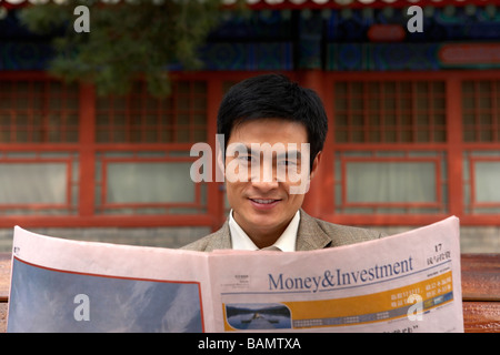 Businessman sitting on a park bench lire le journal Banque D'Images