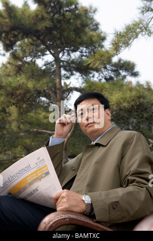 Businessman sitting on a park bench lire le journal Banque D'Images