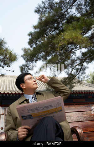 Businessman sitting on a park bench lire le journal Banque D'Images