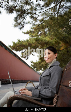 Businesswoman sitting on a park bench en utilisant son ordinateur portable Banque D'Images