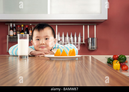 Jeune garçon boire du lait et manger des oranges Banque D'Images