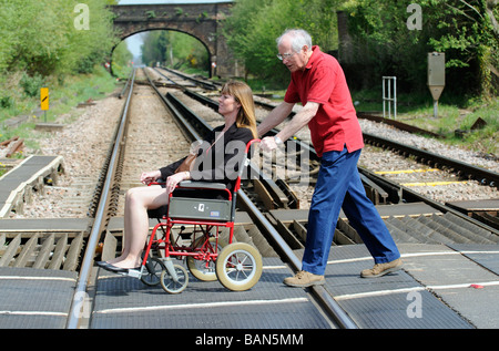 Une manœuvre de soignant masculin style transit fauteuil roulant et femme handicapée sur un passage à niveau Banque D'Images