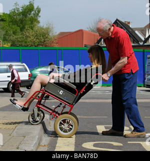 Une manœuvre de soignant masculin style transit fauteuil roulant et à mobilité réduite d'un trottoir en bordure de la femme Banque D'Images