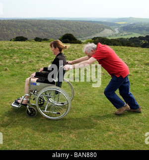 Carer poussant femme dans un fauteuil roulant dans la campagne anglaise UK Banque D'Images