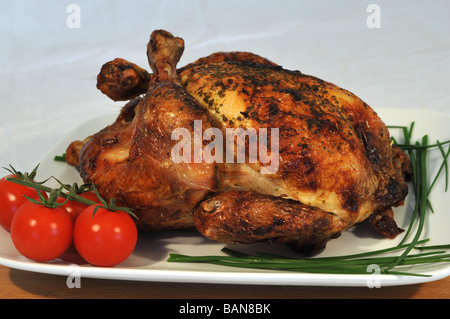 Poulet rôti le dîner servi sur une plaque blanche et décoré avec des tomates et de la ciboulette. Banque D'Images