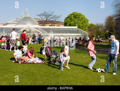 Des groupes de personnes bénéficiant d'une belle journée de printemps sur une pelouse en face de Kibble Palace dans le jardin botanique. Banque D'Images