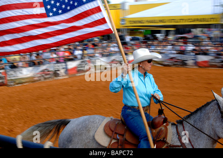 Cowgirl sur les courses de chevaux par la foule dans l'arène de rodéo pendant l'affichage de l'étoile et les bars ou le drapeau de l'United States Banque D'Images