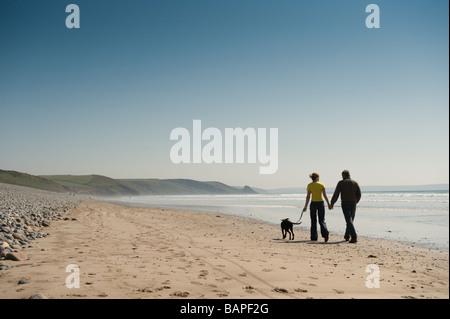 Un jeune couple en train de marcher de pair avec leur chien de compagnie sur la plage de Newgale Galles Pembrokeshire Coast national park après-midi d'été Banque D'Images